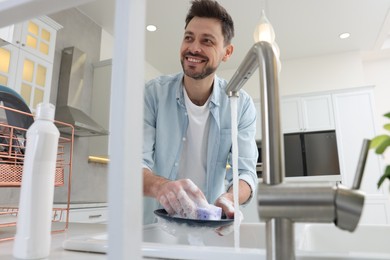 Man washing plate above sink in kitchen, view from outside