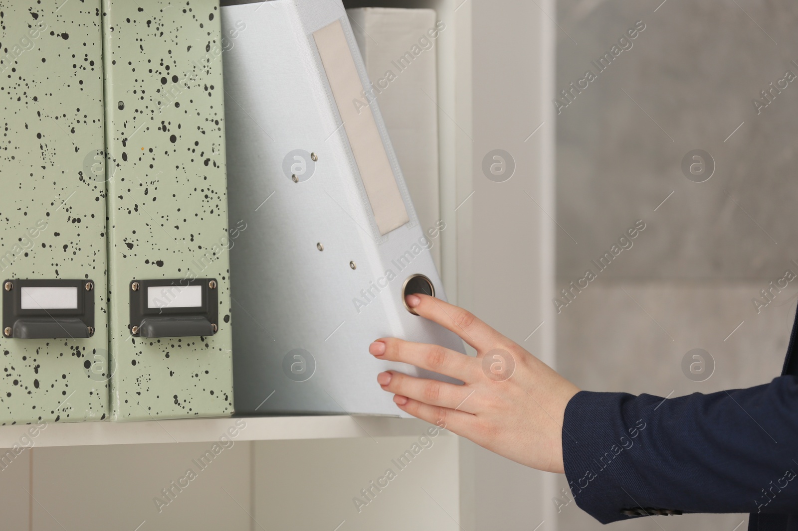 Photo of Woman taking folder with documents from shelf in office, closeup