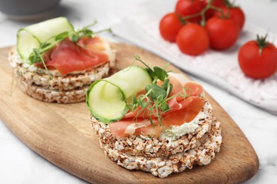 Photo of Crunchy buckwheat cakes with cream cheese, prosciutto and cucumber slices on wooden board, closeup