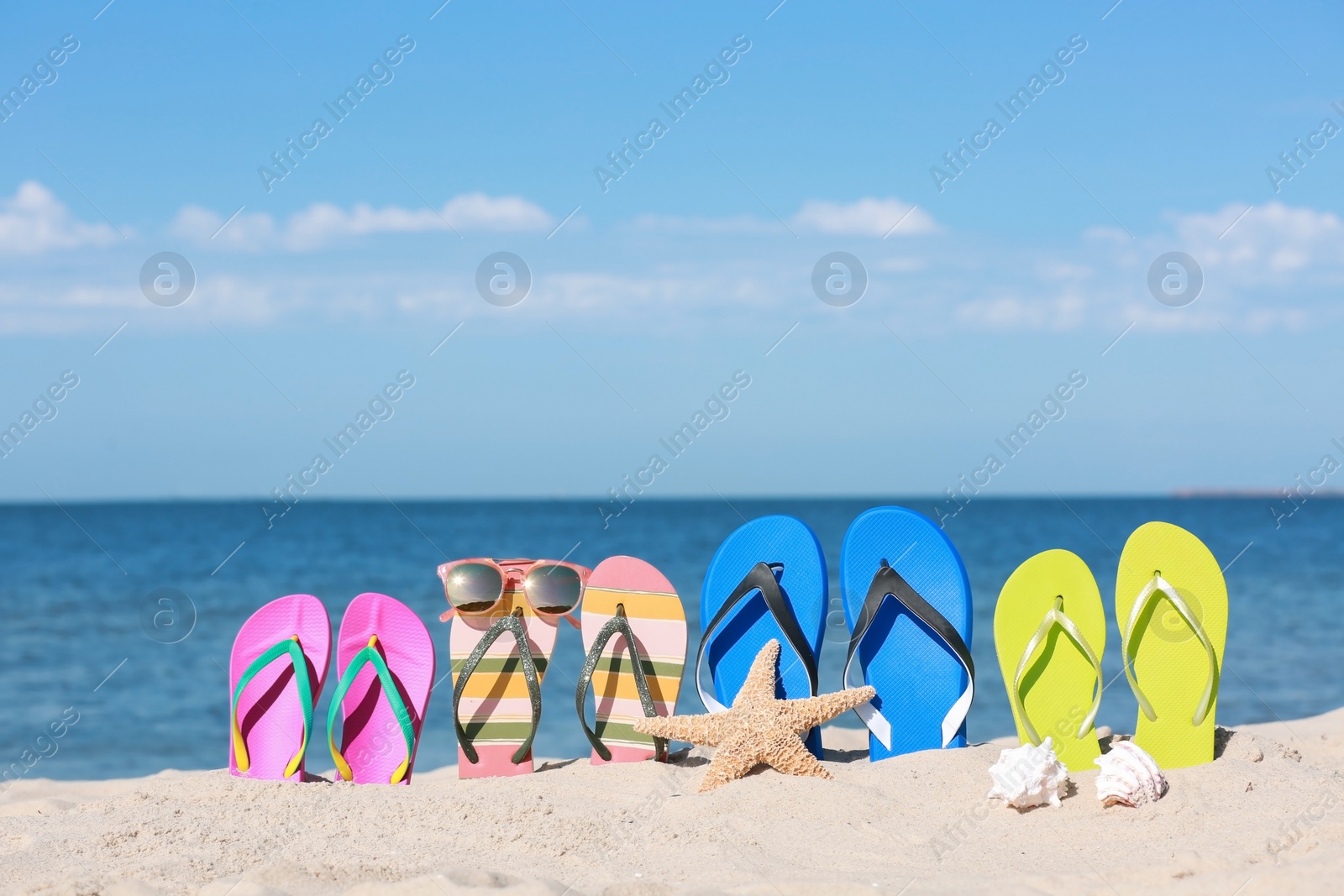 Photo of Composition with bright flip flops on sand near sea in summer. Beach accessories