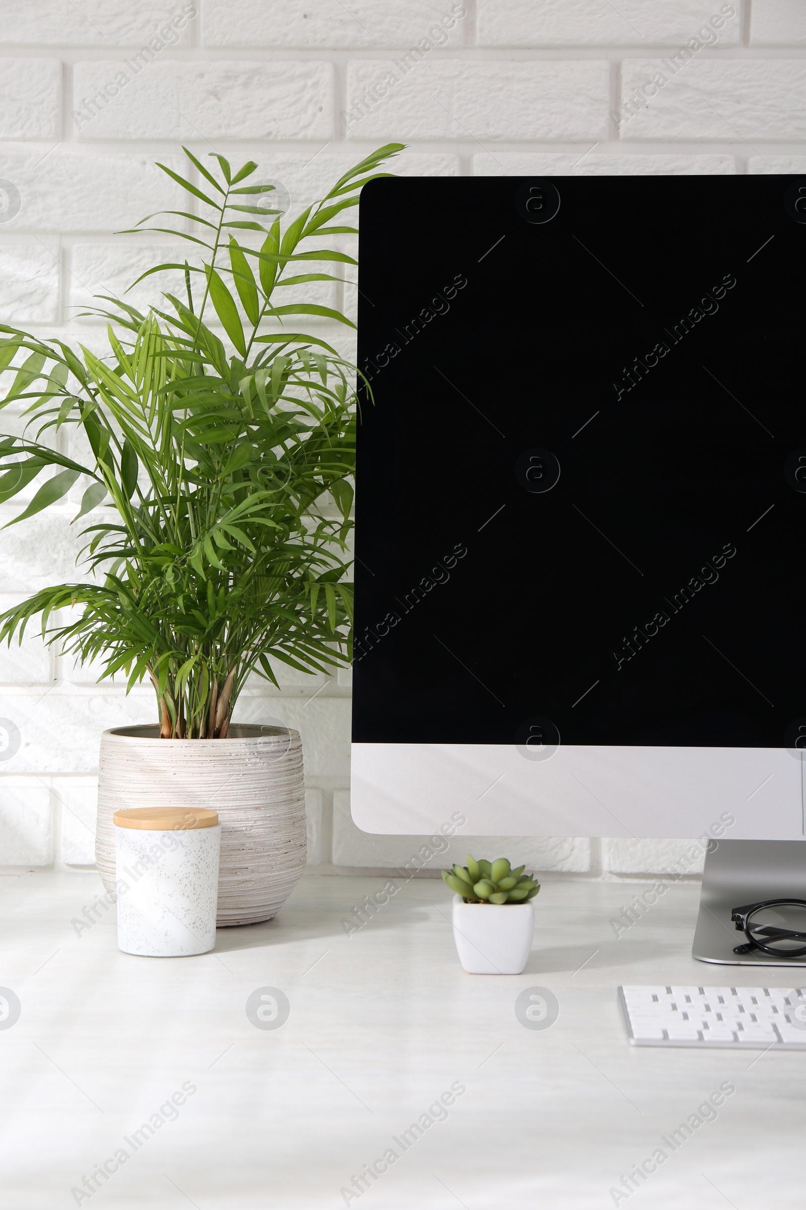 Photo of Office workplace with computer and houseplants on table near white brick wall