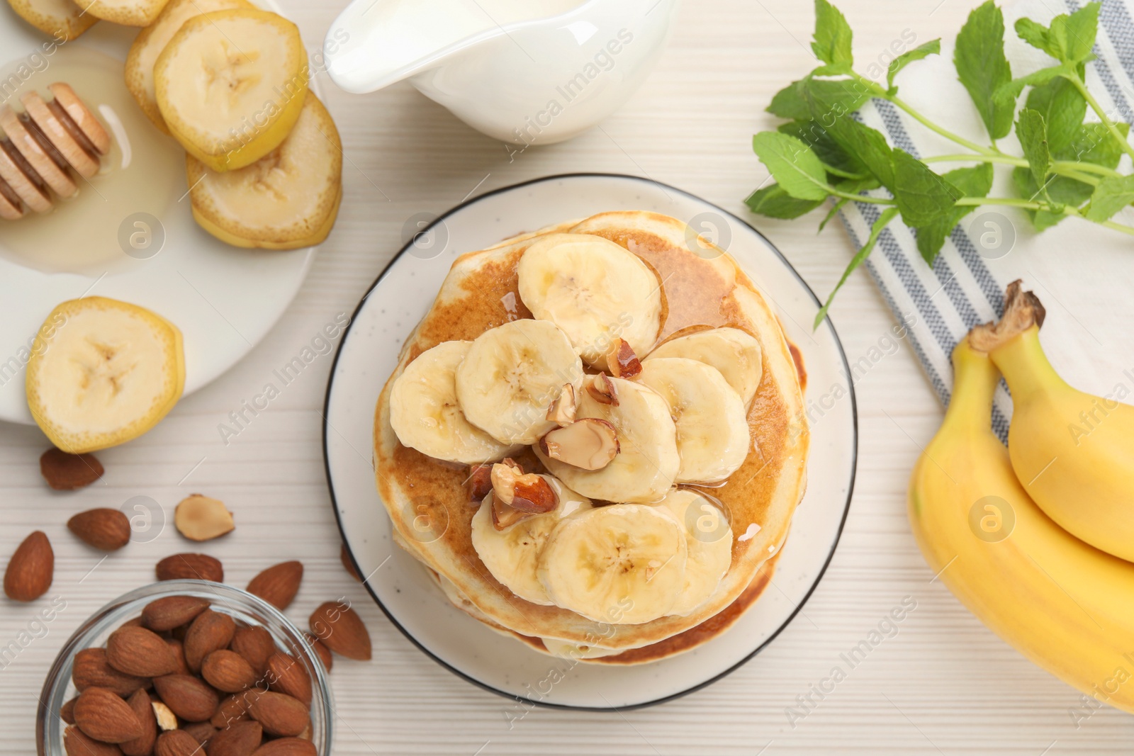 Photo of Tasty pancakes with sliced banana served on white wooden table, flat lay