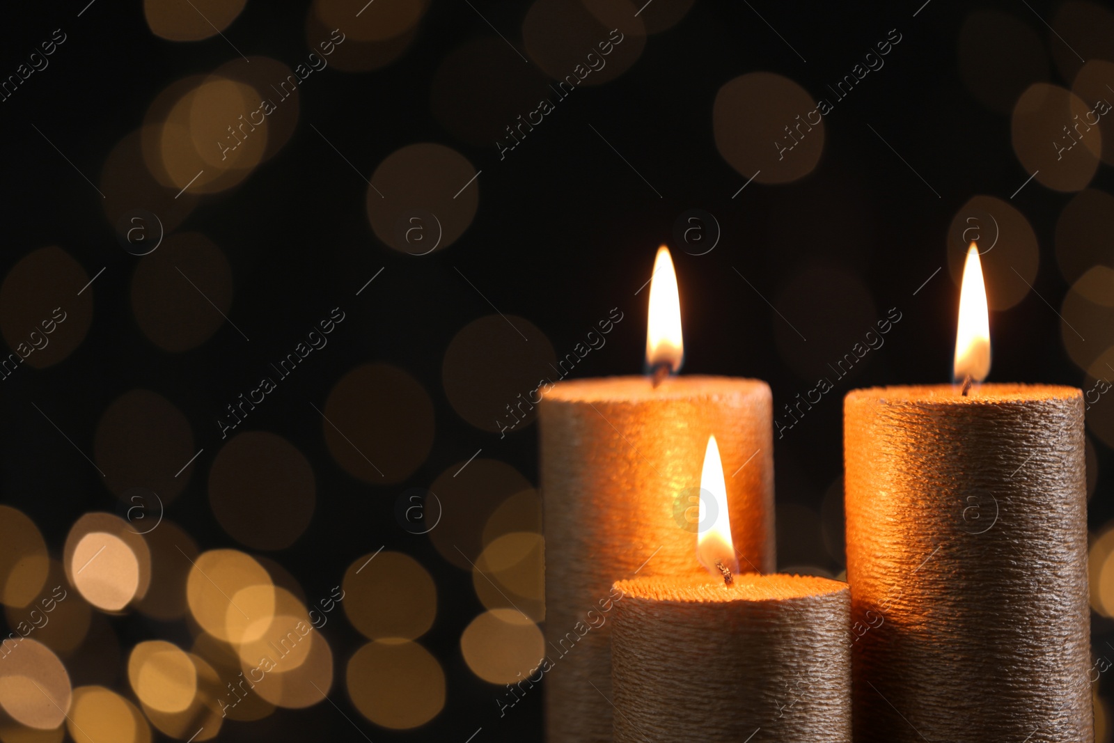 Photo of Burning gold candles against blurred lights in darkness. Space for text