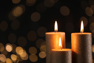 Burning gold candles against blurred lights in darkness. Space for text