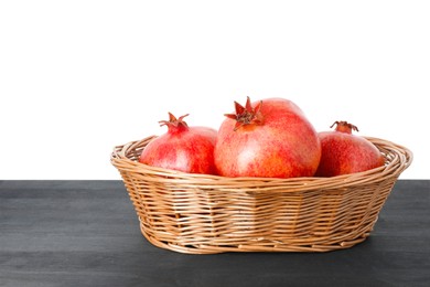 Photo of Fresh pomegranates in wicker basket on black wooden table against white background