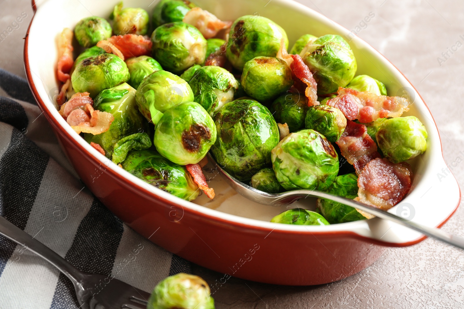 Photo of Delicious Brussels sprouts with bacon in baking dish on marble table, closeup