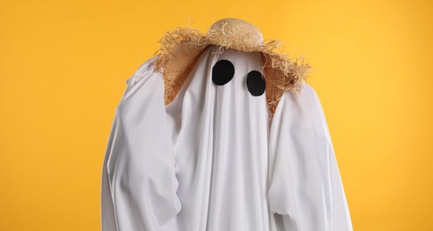 Person in ghost costume and straw hat on yellow background