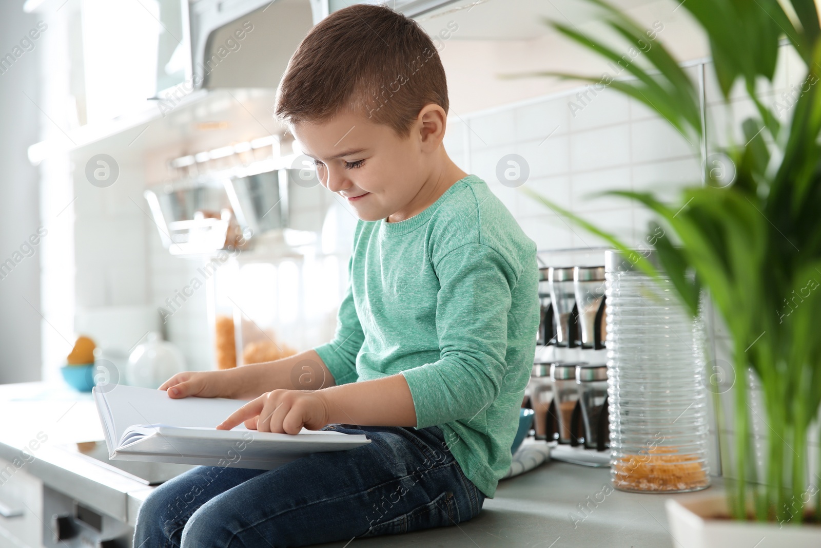 Photo of Cute little boy reading book in kitchen at home