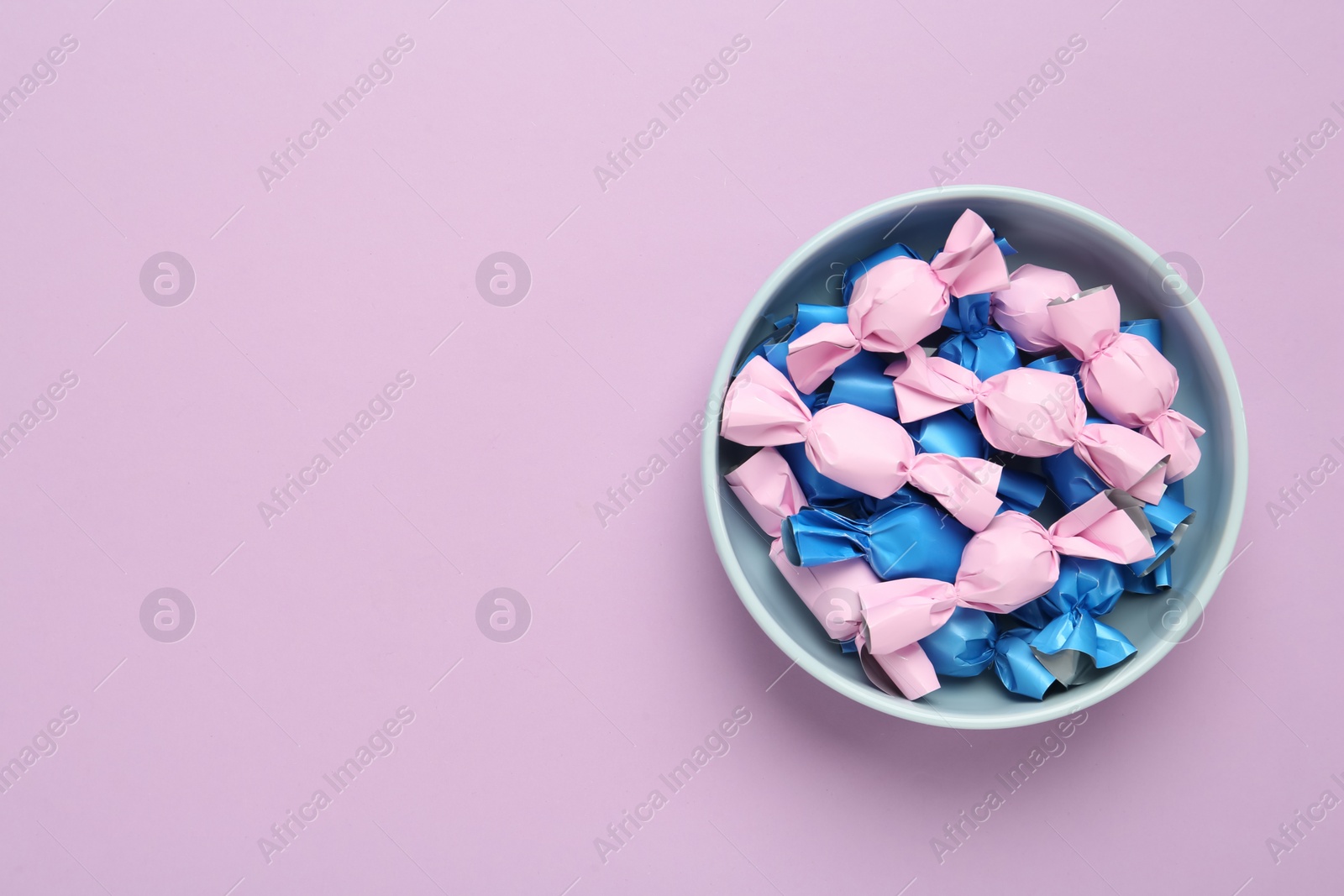 Photo of Candies in colorful wrapper on pink background, top view. Space for text