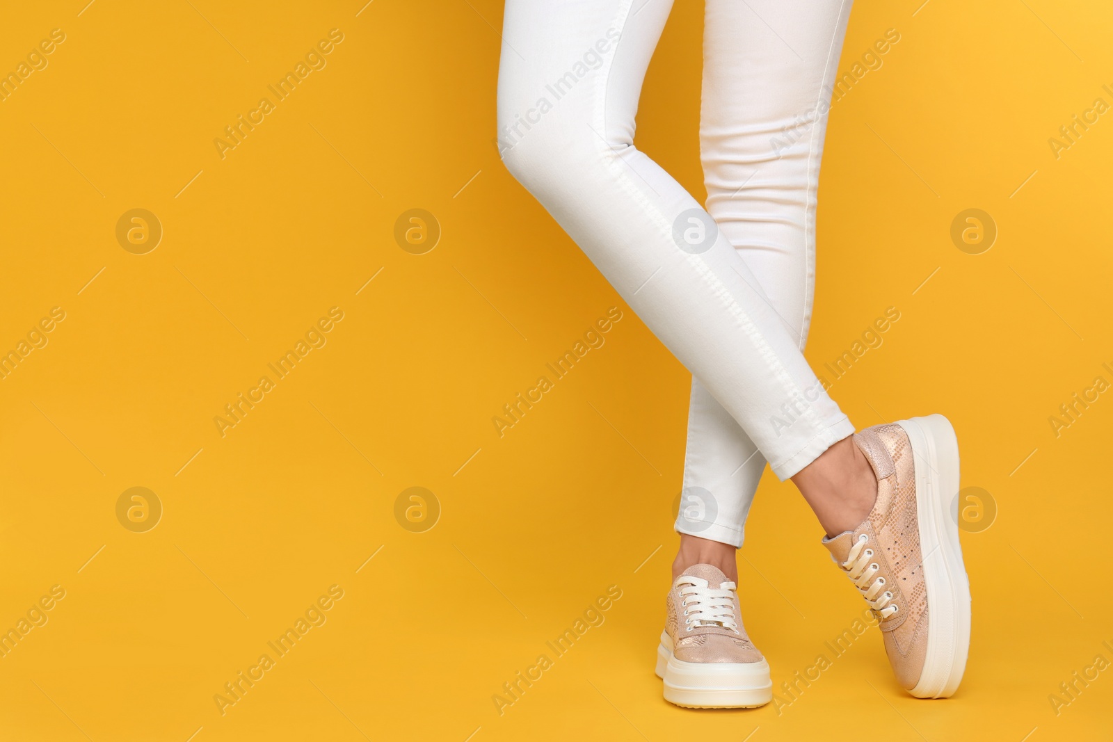 Photo of Woman wearing stylish shoes on yellow background, closeup. Space for text