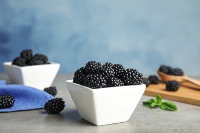 Bowls of tasty blackberries on grey table against blue background