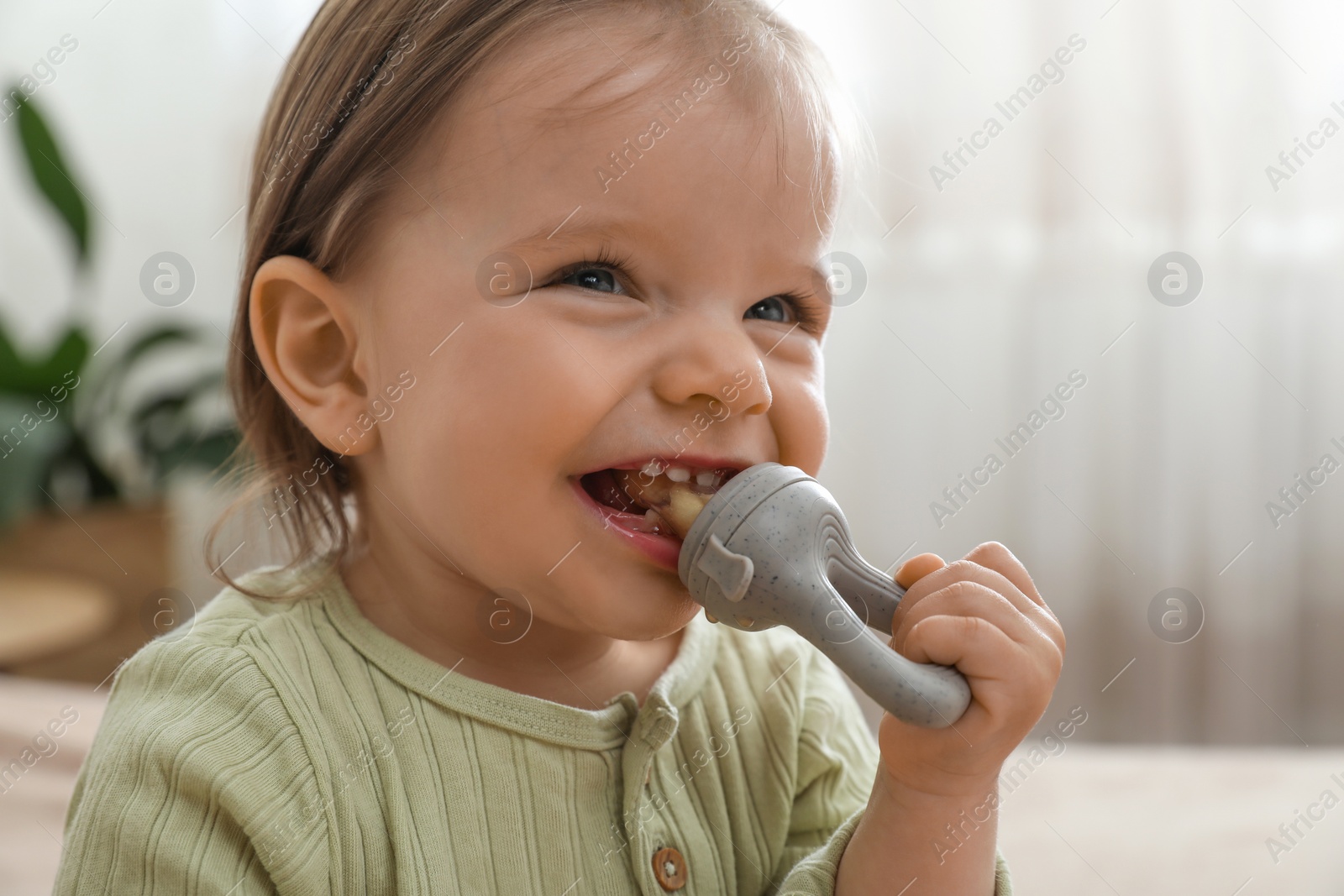 Photo of Cheerful baby girl with nibbler at home, closeup