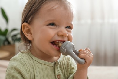 Photo of Cheerful baby girl with nibbler at home, closeup