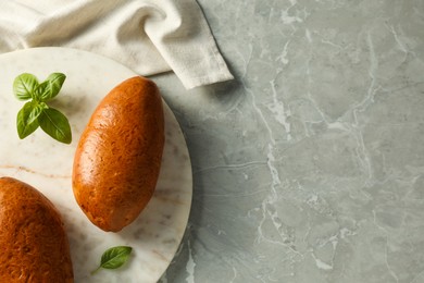 Photo of Tasty freshly baked pirozhki and basil on light grey marble table, top view. Space for text