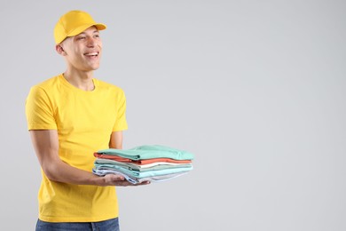 Photo of Dry-cleaning delivery. Happy courier holding folded clothes on light grey background, space for text