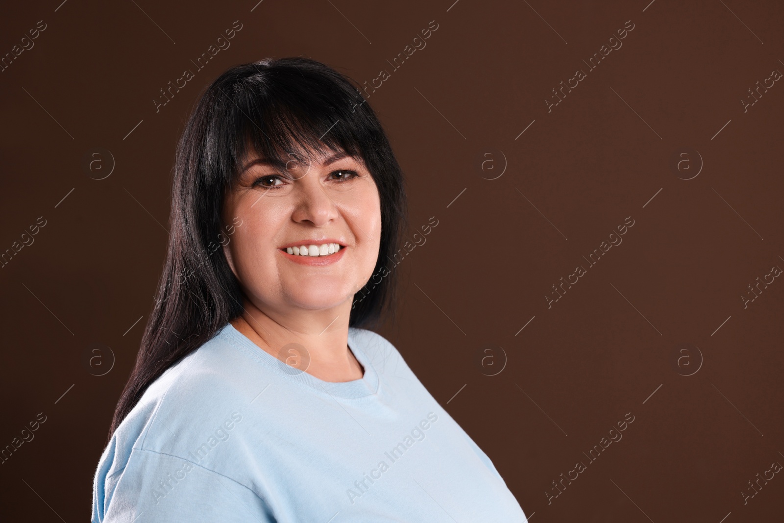 Photo of Beautiful overweight mature woman with charming smile on brown background. Space for text