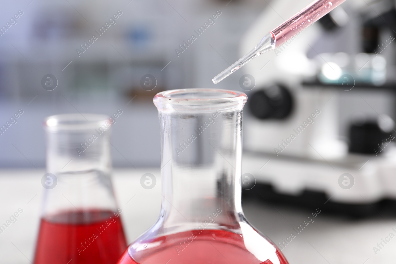 Photo of Laboratory analysis. Dripping red liquid into flask at light grey table, closeup