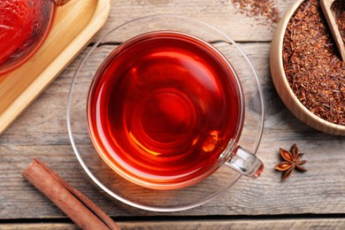 Photo of Freshly brewed rooibos tea, scattered dry leaves and spices on wooden table, flat lay