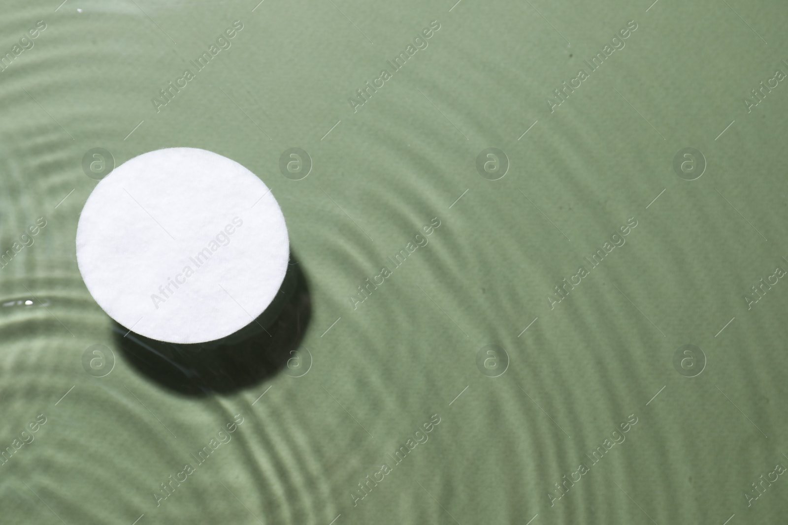 Photo of Cotton pad in micellar water on olive background, top view. Space for text