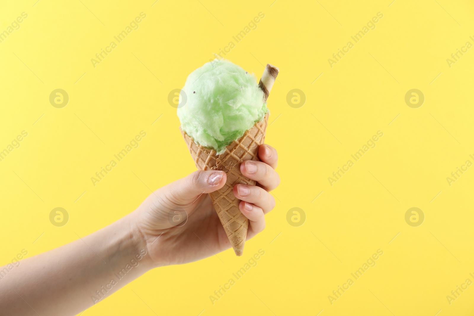 Photo of Woman holding waffle cone with cotton candy on yellow background, closeup