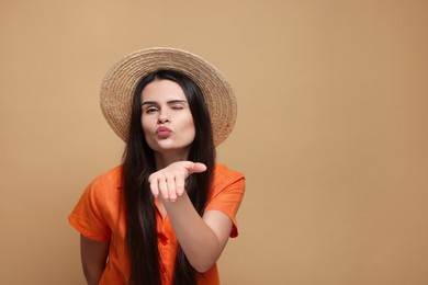 Beautiful young woman in straw hat blowing kiss on beige background. Space for text