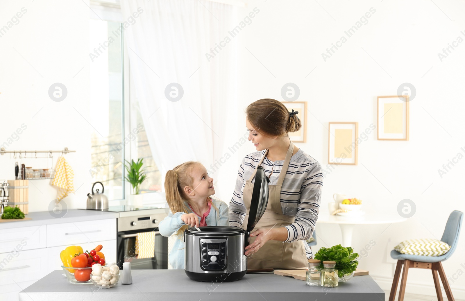 Photo of Mother and daughter preparing food with modern multi cooker in kitchen