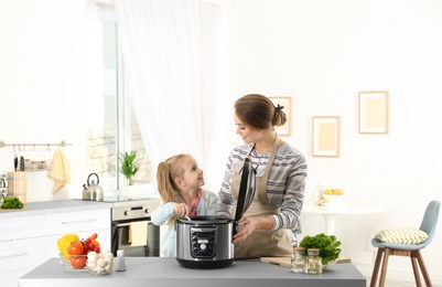 Mother and daughter preparing food with modern multi cooker in kitchen