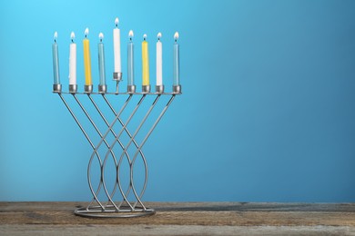 Hanukkah celebration. Menorah with burning candles on wooden table against light blue background, space for text