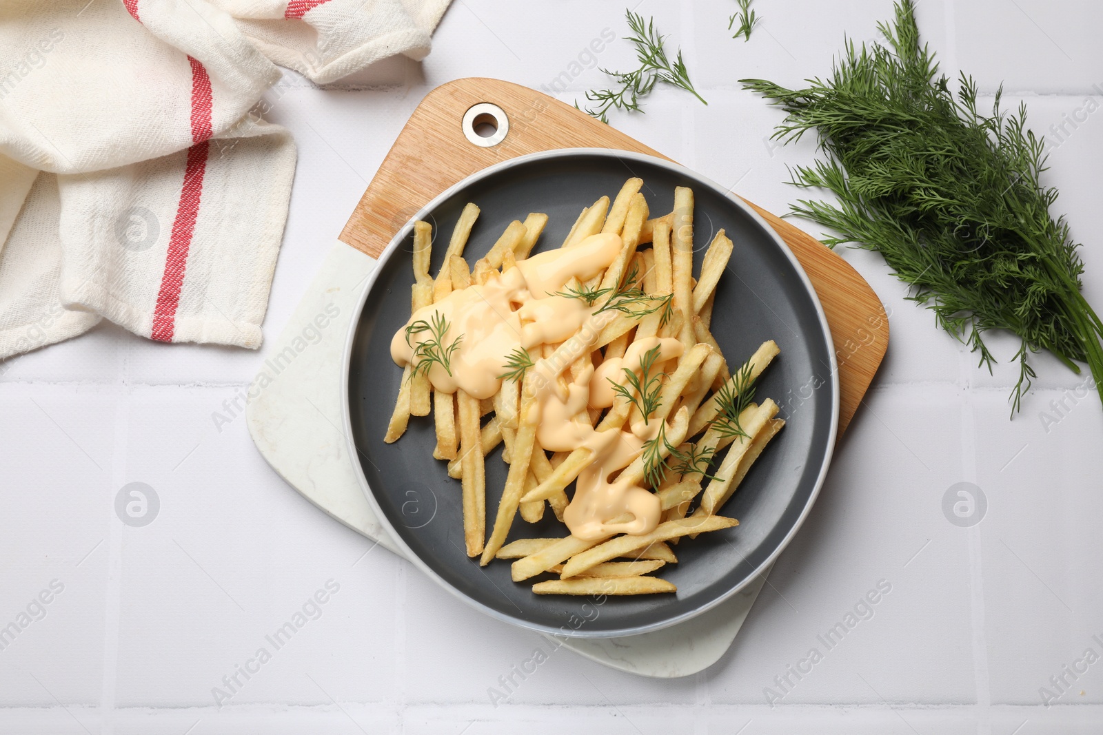 Photo of Delicious french fries with cheese sauce and dill on white tiled table, flat lay