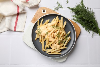 Delicious french fries with cheese sauce and dill on white tiled table, flat lay