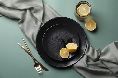 Stylish table setting. Plates, cutlery and tea with lemon on olive background, flat lay