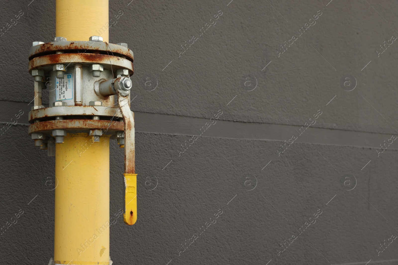 Photo of Yellow gas pipe with valve near brown wall outdoors, space for text