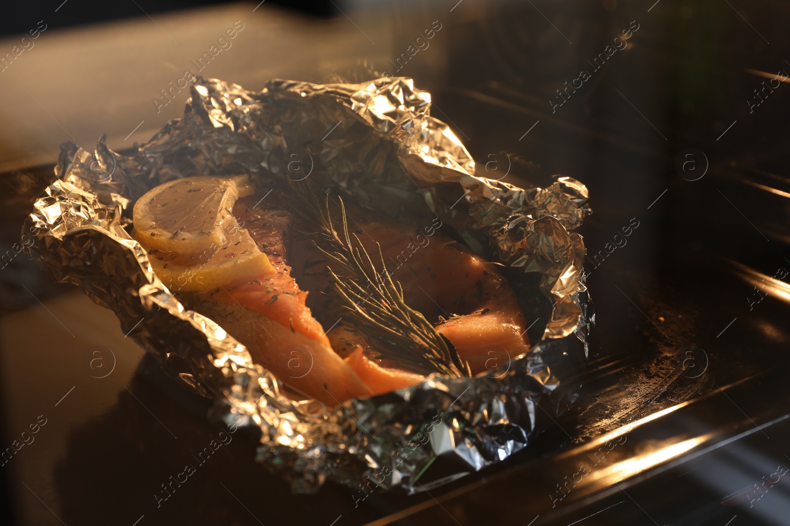 Photo of Foil with fish in oven, closeup. Baking salmon