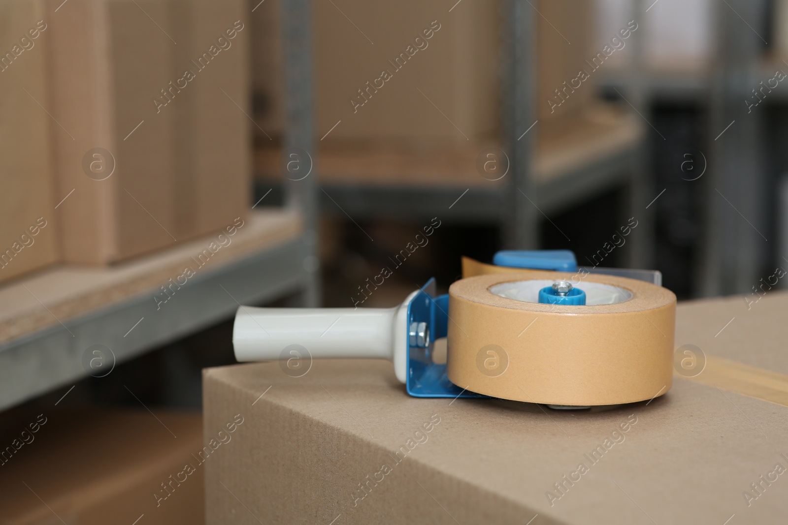 Photo of Adhesive tape dispenser on cardboard box indoors