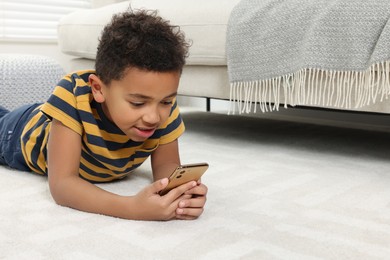 Photo of Cute African-American boy playing on phone at home. Space for text