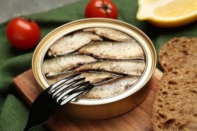 Photo of Canned sprats, fork and bread on table, closeup