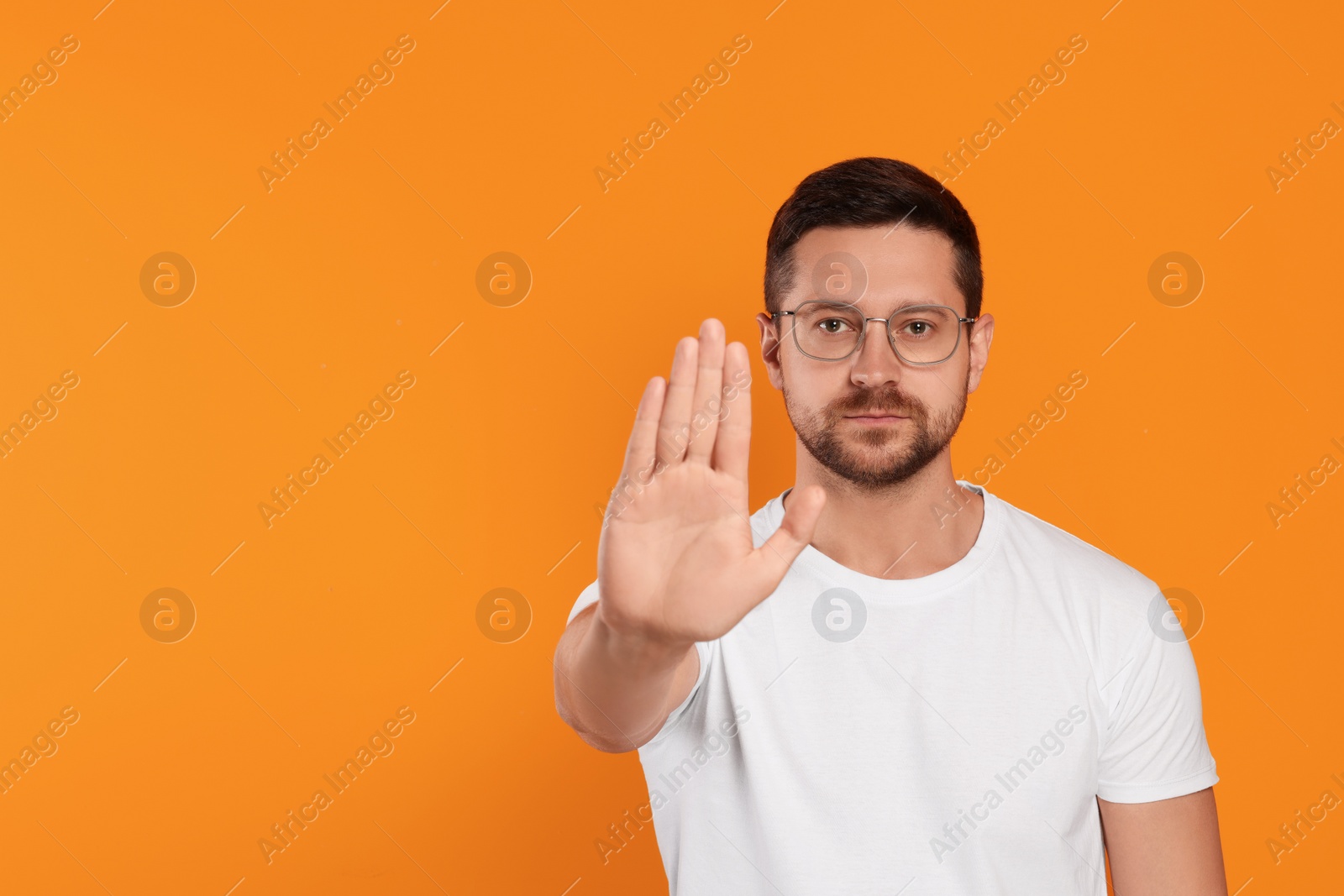 Photo of Handsome man showing stop gesture on orange background, space for text