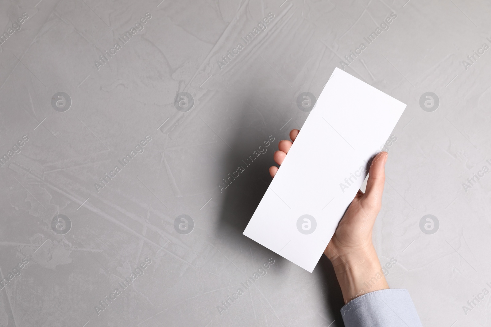 Photo of Woman holding blank card at light grey table, top view. Mockup for design
