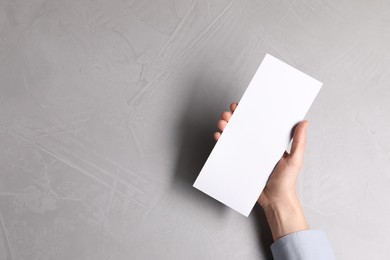 Woman holding blank card at light grey table, top view. Mockup for design