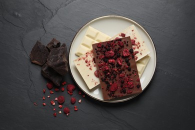 Photo of Chocolate bars with freeze dried fruits on black table, flat lay