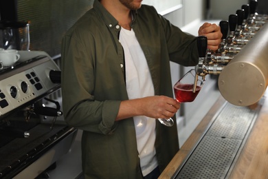 Photo of Bartender pouring fresh beer into glass in pub, closeup