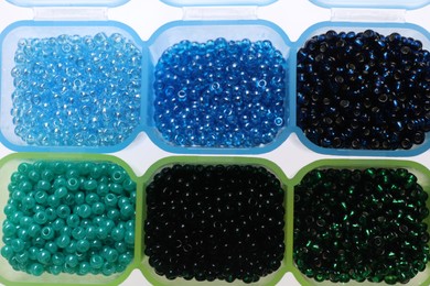 Plastic organizers with different beads on white background, top view