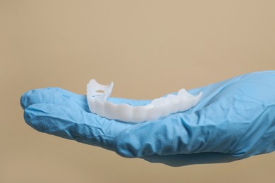 Photo of Bite correction. Dentist in medical glove holding mouth guard on beige background, closeup