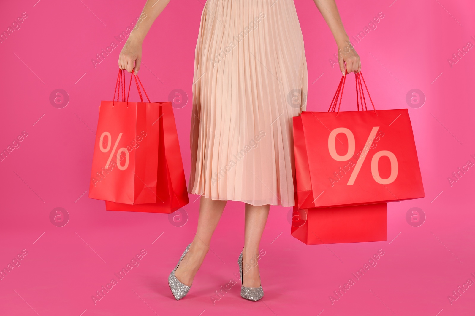 Image of Discount, sale, offer. Woman holding paper bags with percent signs against pink background, closeup