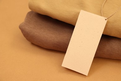 Garment with cardboard tag on kraft paper sheet, closeup. Space for text