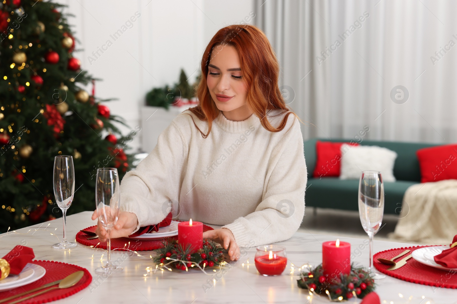 Photo of Beautiful young woman setting table in room decorated for Christmas
