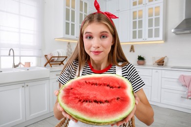 Beautiful teenage girl with half of watermelon in kitchen