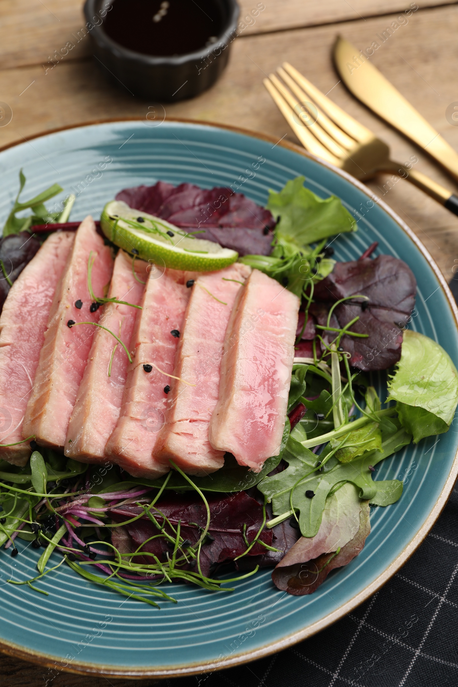 Photo of Pieces of delicious tuna steak with salad served on wooden table, closeup