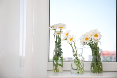 Photo of Vases with beautiful chamomile flowers on windowsill