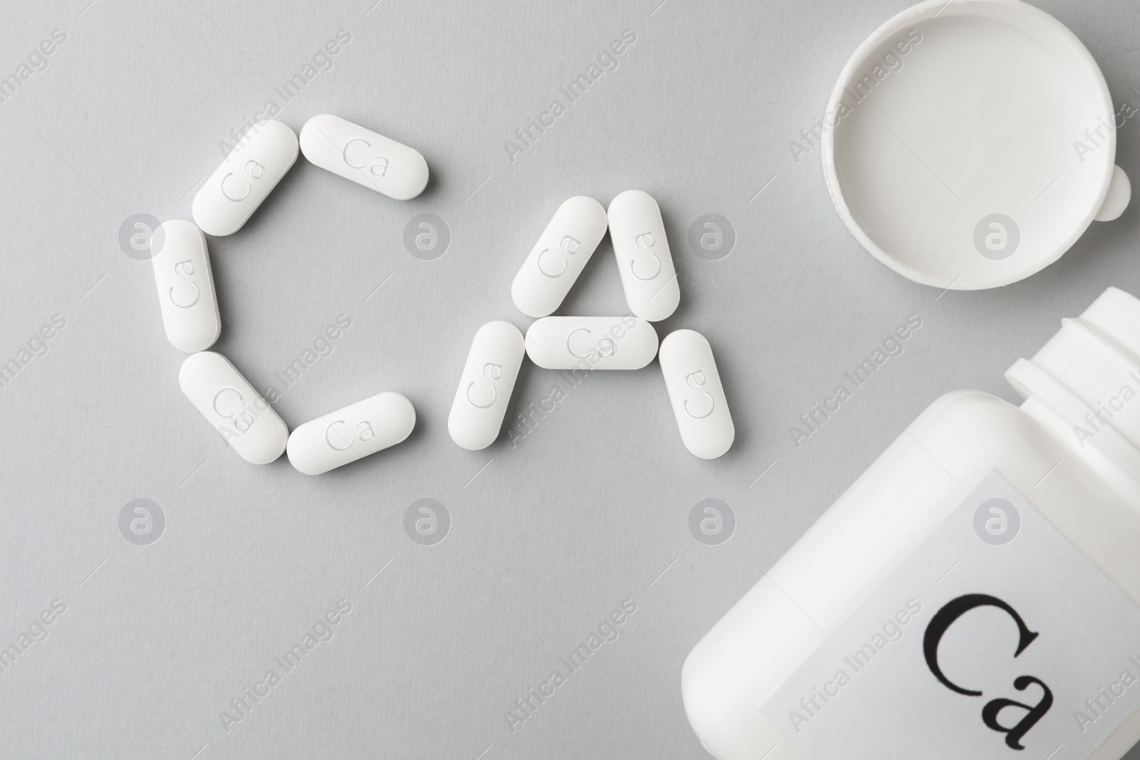 Photo of Calcium supplement pills and jar on light grey background, flat lay